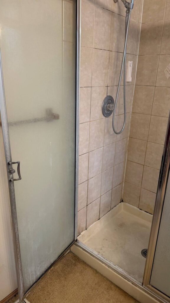 Shower door glass clouded white with mineral scale and a gray shower pan before JenyClean move-out cleaning in Bellevue, WA