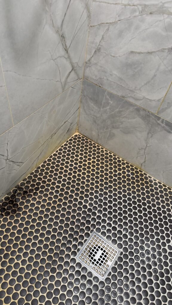 Black penny mosaic shower floor with yellowed grout, soap film and hair near the drain before JenyClean shower deep cleaning in Bellevue, WA