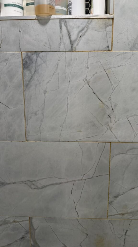 Marble-look shower wall tile with yellow-orange grout lines and splash marks below the niche before JenyClean deep cleaning in Bellevue, WA