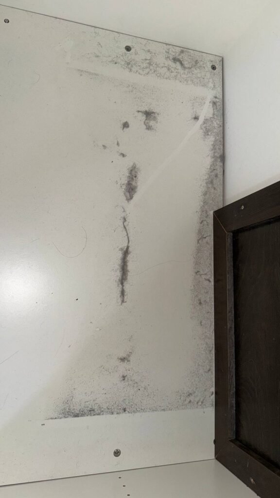 White under-sink cabinet panel with dark mildew spots and streaks before JenyClean deep cleaning in Bothell, WA