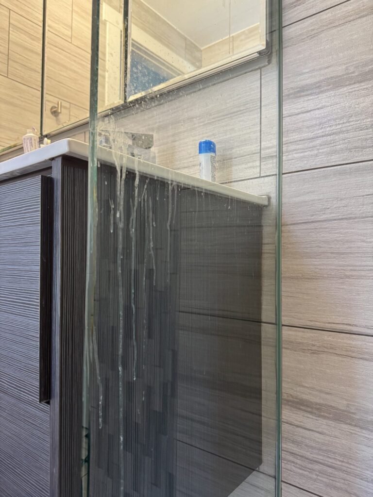 Glass shower partition with dried drip streaks next to a vanity before JenyClean deep cleaning in Issaquah, WA
