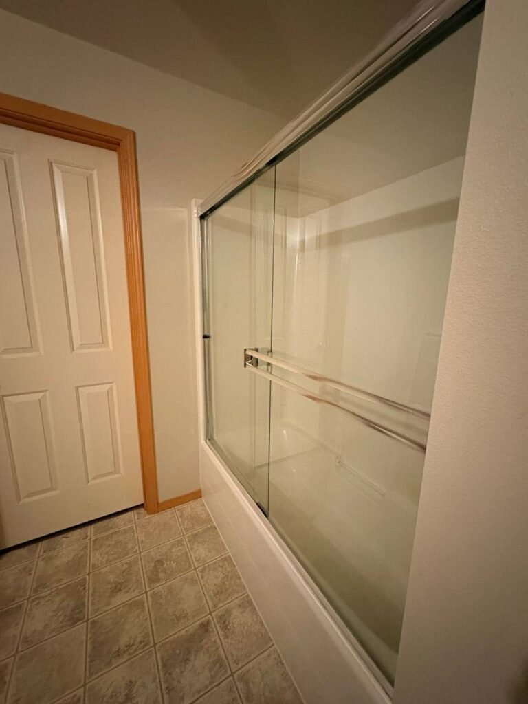 Clear sliding glass shower door with the tub wall visible through it after JenyClean standard cleaning in Issaquah, WA