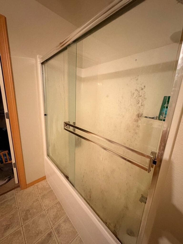 Sliding glass shower door covered in solid white film and dark spots before JenyClean standard cleaning in Issaquah, WA