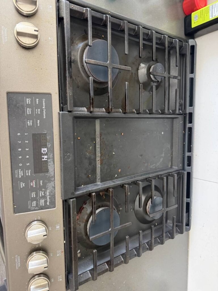 Gas cooktop with crumbs, grease spots and burnt food on the burner pans and center griddle before JenyClean deep cleaning in Issaquah, WA