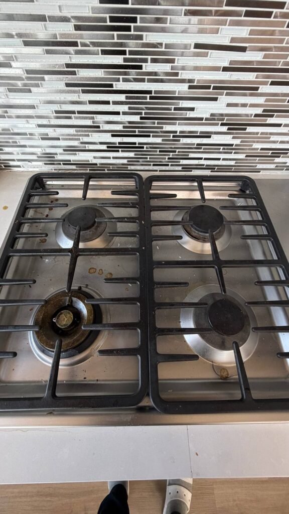 Stainless steel gas cooktop with food spills, grease spots and crumbs around the burners before JenyClean cleaning after guests in Kirkland, WA