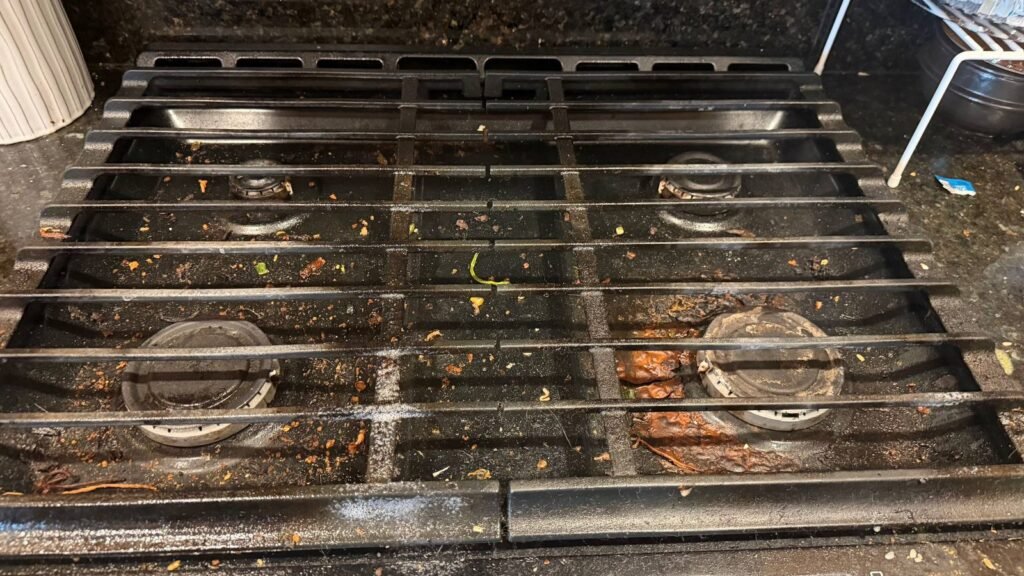 Cast-iron gas cooktop grates with crumbs and baked-on grease before JenyClean kitchen deep cleaning in Kirkland, WA