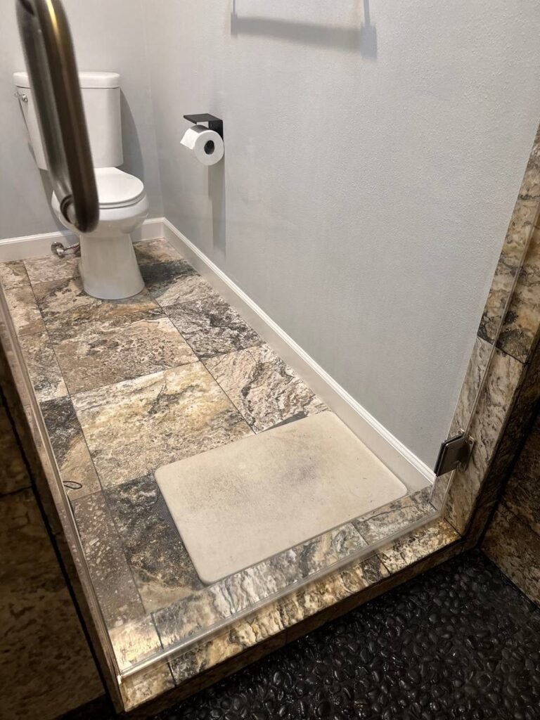 Clear shower glass and clean stone-look threshold above a black pebble floor after JenyClean bathroom deep cleaning in Redmond, WA