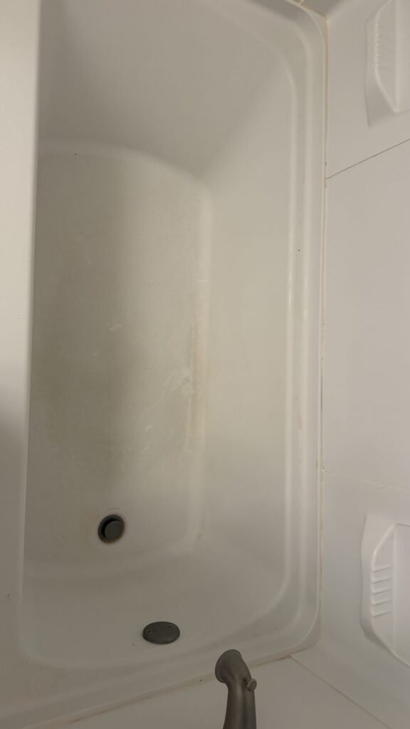 White bathtub with gray soap film, scuff marks and a stained caulk seam before JenyClean regular cleaning in Renton, WA