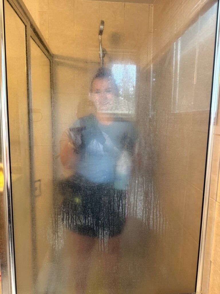 Glass shower enclosure covered in white hard-water film with the cleaner barely visible behind it before JenyClean bathroom cleaning in Sammamish, WA