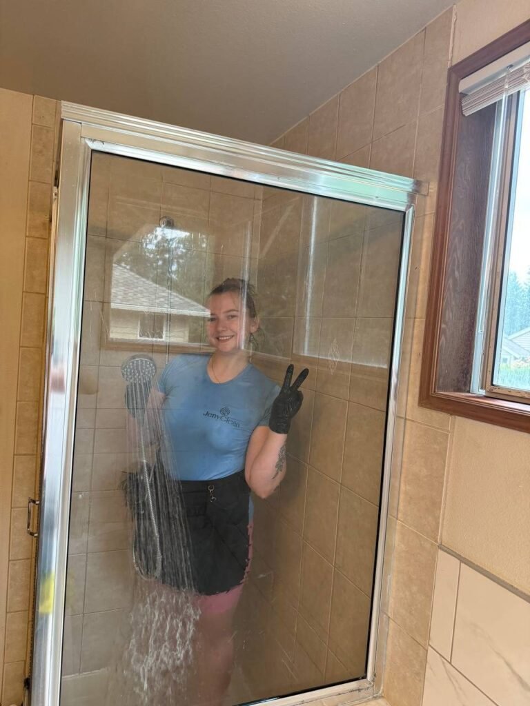Cleaner rinsing the inside of a glass shower enclosure with a hand shower during JenyClean bathroom cleaning in Sammamish, WA