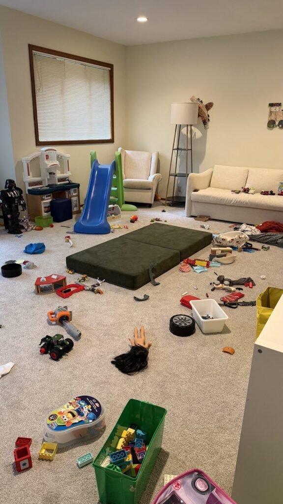 Play mattress, toy vehicles, a doll and a bin of building bricks on the playroom carpet before JenyClean organizing in Sammamish, WA