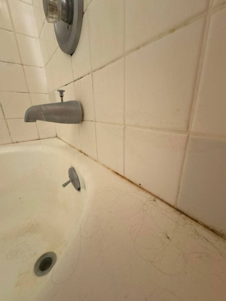 Bathtub with hair near the drain and dark spots in the tile grout before JenyClean cleaning in Seattle, WA