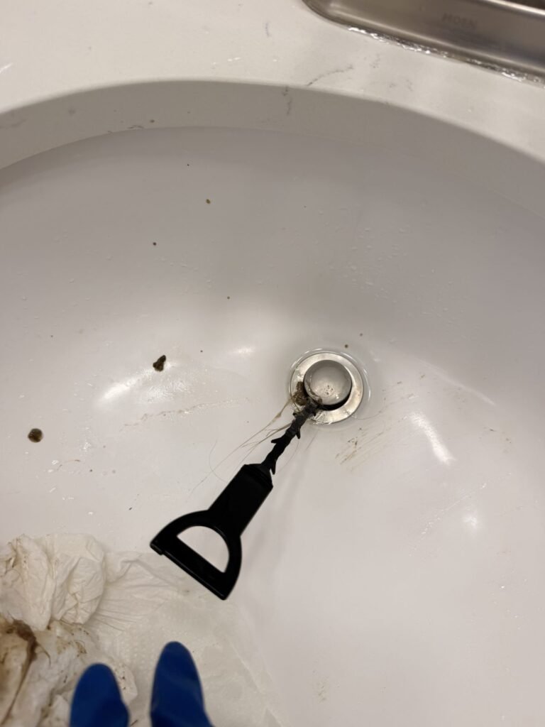 Plastic drain hook inserted beside the pop-up stopper of a bathroom sink during JenyClean deep cleaning in Seattle, WA