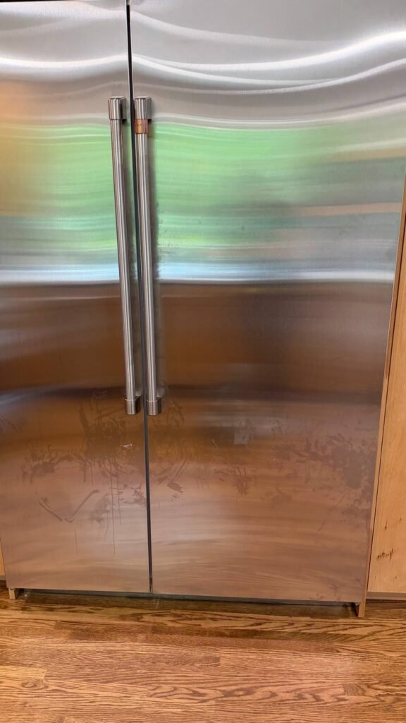 Stainless fridge doors with curved streaks from a damp cloth below the handles before JenyClean cleaning in Seattle, WA