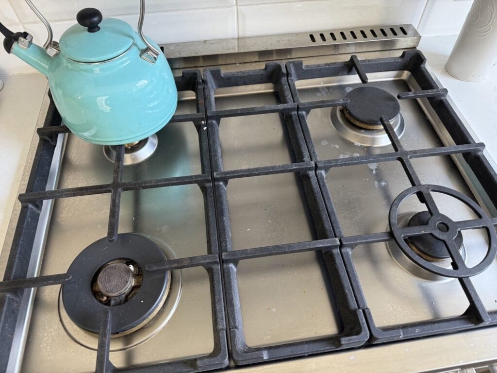Stainless gas cooktop with cast-iron grates, spills and burnt residue before JenyClean deep cleaning in Seattle, WA