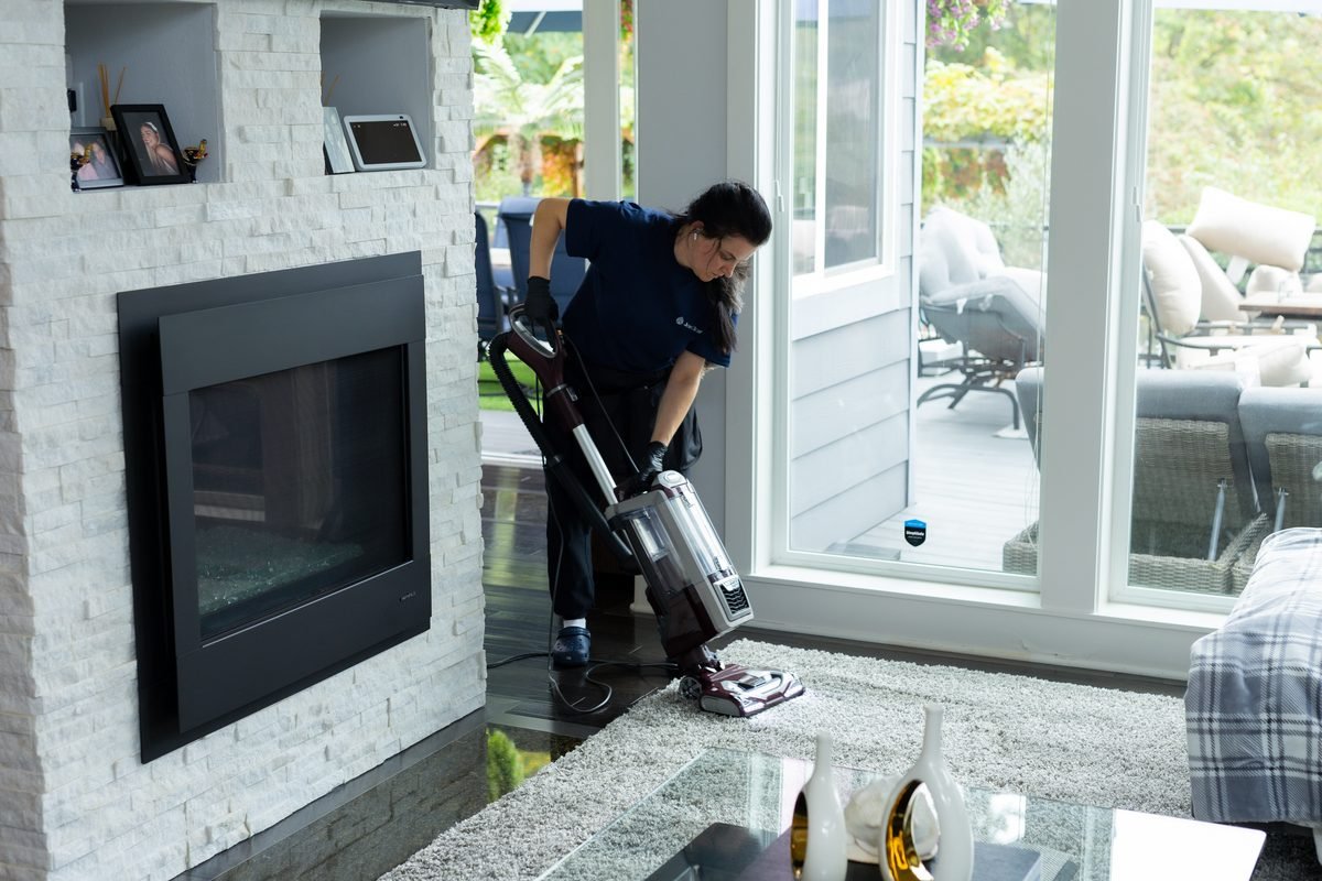House cleaning in Sammamish: JenyClean cleaner vacuuming a living room rug by the fireplace